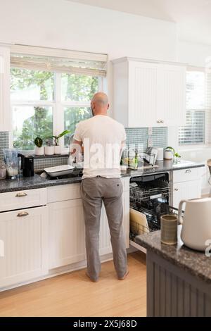 Mann, der in der sonnigen Küche Geschirr tut Stockfoto