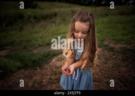 Schönes kleines Mädchen mit langen Locken, das draußen einen kleinen Frosch hält Stockfoto