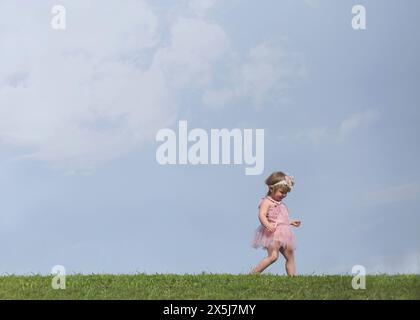 Kleines blondes Mädchen in rosa Kleid, das in den Wolken erforscht Stockfoto