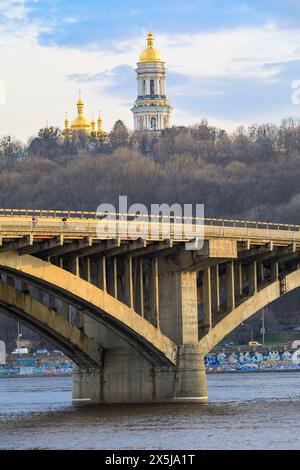 Ukraine, Kiew, Kiew. Metro Bridge über den Dnieper River. Dächer des Klosters der Höhlen (Petschersk Lavra) im Hintergrund. Stockfoto