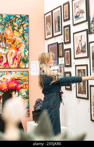 Frau arrangiert Bilderrahmen an der Wand auf der Kunstmesse. Stockfoto