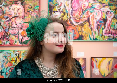 Junge Frau mit Hut, die Gemälde am Eröffnungstag der Kunstmesse beobachtet. Stockfoto