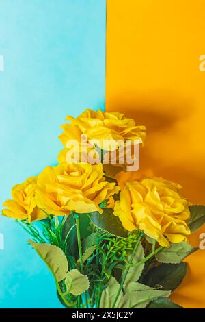 Strauß aus gelben Rosen auf blauem und gelbem Hintergrund. Vertikale Aufnahme, Draufsicht. Stockfoto