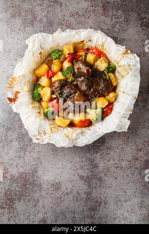 Lamm in eigenem Saft gekocht mit Gemüse und Kräutern in Pergament Nahaufnahme in einer Pfanne auf dem Tisch. Vertikale Draufsicht von oben Stockfoto