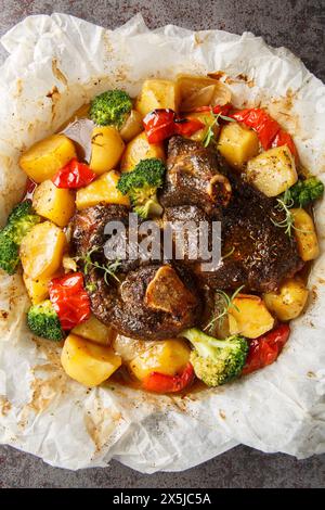 Langsam gekochtes Lamm mit Kartoffeln, Brokkoli, Zwiebeln und Paprika in Backpapier in einer Pfanne auf dem Tisch. Vertikale Draufsicht von oben Stockfoto