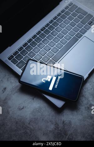 Hohe Ansicht des Smartphones, das auf einem Laptop liegt, mit Entsperrvorgang auf dem Bildschirm. Entsperren Sie das digitale Gerät. Sicherheitsschutzkonzept. Daten vor Hackerangriffen schützen. Stockfoto