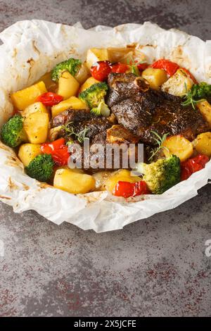 Lamm in eigenem Saft gekocht mit Gemüse und Kräutern in Pergament Nahaufnahme in einer Pfanne auf dem Tisch. Vertikal Stockfoto