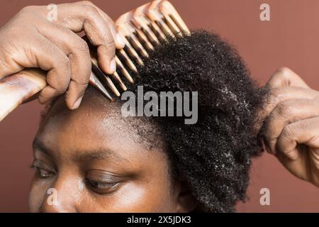 Kämmen Sie schwarzes Afro-lockiges Haar mit Schrumpfung, und entwirren Sie nasses 4c-Haar mit einem breiten Zahnkamm Stockfoto