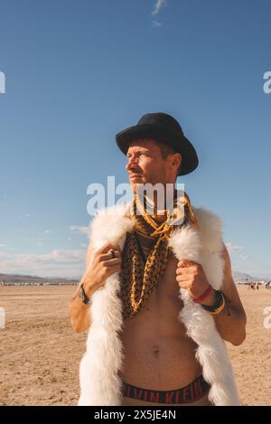 Mann in schwarzem Hut und Pelzkleid beim Outdoor Festival in der Wüste Stockfoto