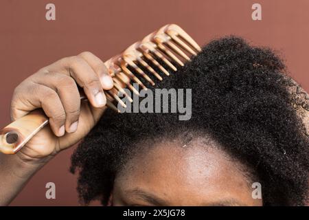 Kämmen Sie schwarzes Afro-lockiges Haar mit Schrumpfung, und entwirren Sie nasses 4c-Haar mit einem breiten Zahnkamm Stockfoto