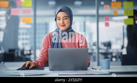 Modernes Büro: Porträt einer jungen muslimischen Geschäftsfrau, die Hijab trägt, arbeitet auf Laptop, macht Datenanalyse, Website-Design, kreative Entwicklung. Digital Entrepreneur arbeitet am E-Commerce Startup Project Stockfoto