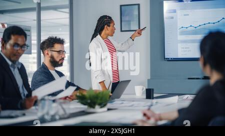 Diversity Modern Office: Schwarze Geschäftsfrau leitet Geschäftstreffen mit Managern, spricht, erklärt Statistiken, verwendet Präsentationsfernsehen mit Diagrammen, Big Data. Digitale Unternehmer arbeiten am eCommerce-Projekt Stockfoto