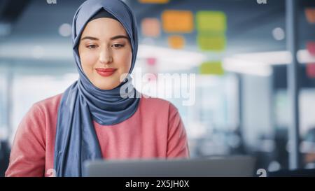 Modernes Büro: Porträt einer jungen muslimischen Geschäftsfrau, die Hijab trägt, arbeitet auf Laptop, macht Datenanalyse, Website-Design, kreative Entwicklung. Digital Entrepreneur arbeitet am E-Commerce Startup Project Stockfoto