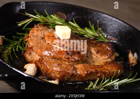 Schweinekotelett auf dem Knochen in einem Stück Butter mit Knoblauch und Rosmarin in einer Pfanne Stockfoto