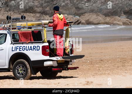 Ein RNLI-Rettungsschwimmer steht auf seinem Rettungswagen, der am Fistral Beach in Newquay in Cornwall in Großbritannien geparkt ist. Stockfoto