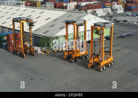 Drei orangene Straßenbahnträger im Bridgetown Containerterminal parken in der Nähe von Lagerhallen und Portalkranen. Stockfoto