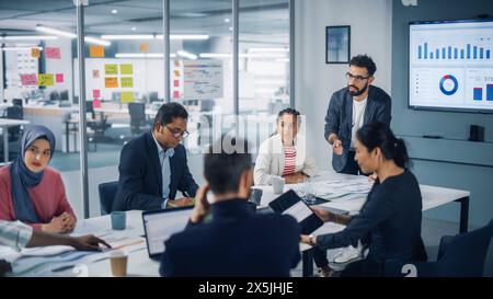 Vielfältiges modernes Büro: Geschäftsmann leitet Geschäftstreffen mit Managern, spricht, nutzt Präsentationsfernsehen mit Statistiken, Infografiken. Digitale Unternehmer arbeiten am E-Commerce-Projekt. Stockfoto