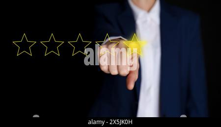 Mann, der einen von fünf Sternen auf dem virtuellen Bildschirm vor schwarzem Hintergrund auswählt, Nahaufnahme. Bewertung der Kundenzufriedenheit, Bannerdesign Stockfoto