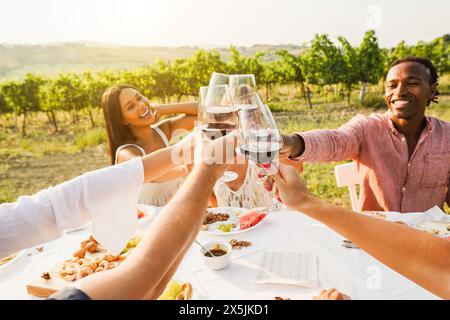 Glückliche Erwachsene Freunde, die Spaß dabei haben, Rotwein zu trinken und zusammen mit dem Weingut im Hintergrund zu essen - multirassische Leute, die im Sommer Vorspeisen essen Stockfoto