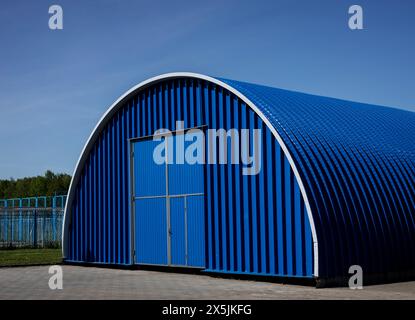 Blaues Metall-Hangar, Oval gegen Himmel. Metallkonstruktion des Industriegebäudes im Freien. Stockfoto