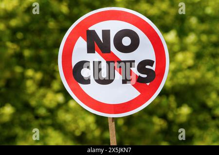 Bei einem Protest gegen die Sparpolitik in Bristol ist ein rundes Protestplakat im Stil eines britischen Straßenschilds mit kühner Aufschrift „No Cuts“ abgebildet. Stockfoto