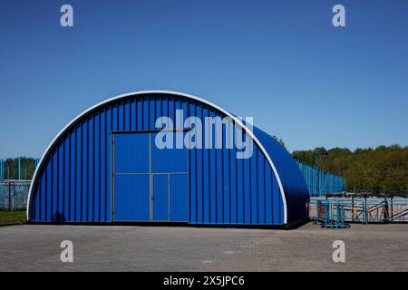 Dach eines Hangars aus blau gerolltem Metall vor dem Hintergrund des Himmels. Metallkonstruktion des Industriegebäudes im Freien. Stockfoto