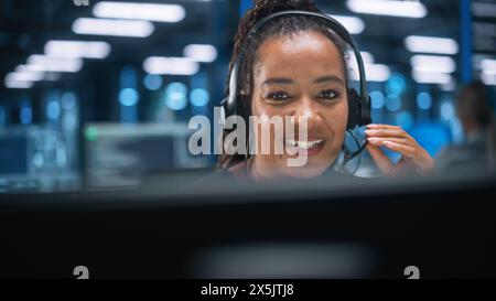 Callcenter-Büro: Porträt einer freundlichen afroamerikanischen Technischen Kundendienstspezialistin, die über Headset spricht und Computer verwendet. Client Experience Officer hilft Online via Videokonferenz Stockfoto