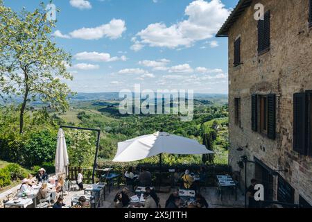 Ein Café und Restaurant am Stadtrand von San Gimignano in der Toskana, Italien an einem sonnigen Frühlingstag, mit herrlichem Blick über die sanften grünen Hügel. Stockfoto