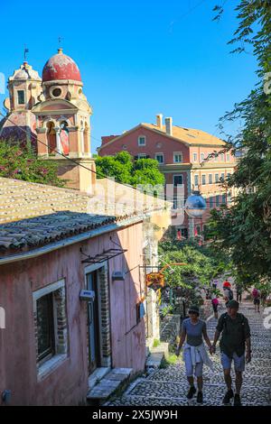 Kerkyra, Korfu, Griechenland. Ein Paar, das Hände hält, spaziert auf Kopfsteinpflasterstraßen vorbei an der alten, rot gewölbten griechischen Kathedrale. (Nur Für Redaktionelle Zwecke) Stockfoto