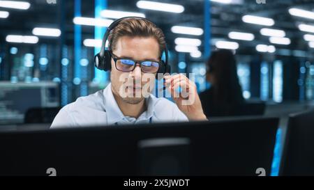 Seriöser junger Kaukasier mit Headset, erfolgreicher Manager des Call Centers sitzt im Büro, verwendet Computer, spricht mit Kunden oder Mitarbeitern über Videokonferenzen. Helpline-Konzept Stockfoto