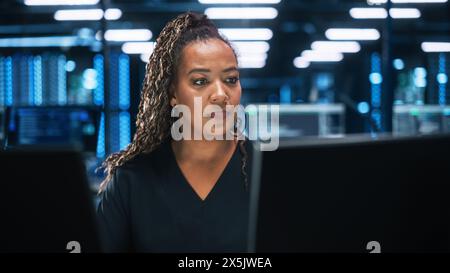 Konzentrierter IT-Spezialist für Computer in Büroumgebungen. Verschiedene multiethnische weibliche Entwicklerinnen verwenden zwei Monitore, während sie spät in der Nacht Code schreiben Stockfoto