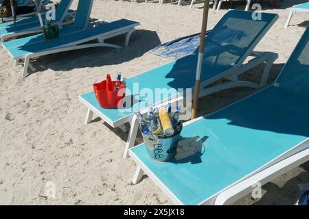 Blassblaue Stühle am Sandstrand, auf denen rote Plastik- und Metalleimer voller leerer Bierflaschen auf Philipsburg stehen. Stockfoto