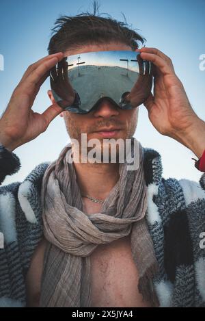 Junger Mann in der Wüste, der die Brille anpasst, Festivalkleidung, Vorfreude. Stockfoto