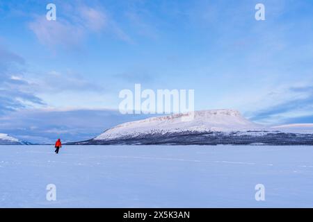 Mann in der arktischen Landschaft spaziert auf der eisigen Oberfläche eines finnischen Sees vor dem Hügel Saana fiel in der Abenddämmerung, Kilpisjarvi, Gemeinde Enontekio, Finni Stockfoto