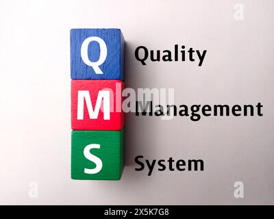 Farbiger Block von oben mit Text QMS (Qualitätsmanagementsystem) auf weißem Hintergrund. Stockfoto