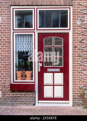 Holland, Niederlande, Schagen. Rot-weiße Tür und Fenster in einem Backsteinhaus im niederländischen Dorf Schagen. (Nur Für Redaktionelle Zwecke) Stockfoto