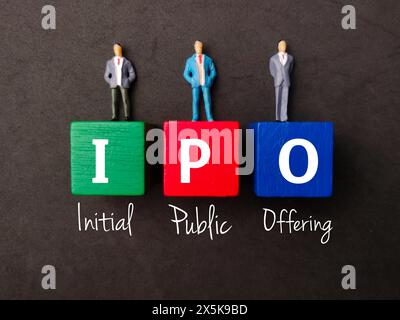 Miniatur-Personen und farbiger Block mit Text IPO (Initial Public Offering) auf schwarzem Hintergrund. Stockfoto