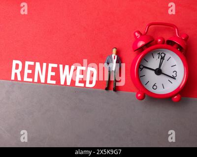 Miniatur-Personen und Uhr mit ERNEUERTEM Text auf rotem und grauem Hintergrund von oben Stockfoto