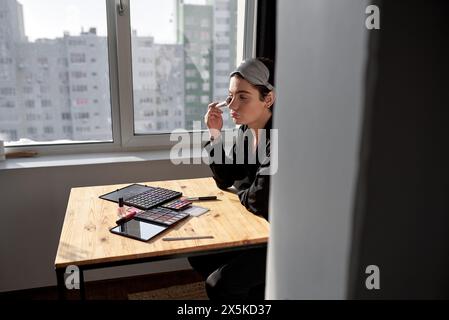 Junger Transgender wendet Kosmetik auf sein Gesicht, Nahaufnahme Seitenporträt, Hautpflege, Schönheitskonzept, Fenster im Hintergrund des Fotos an Stockfoto