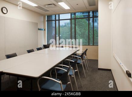 Kleiner leerer Sitzungssaal mit langem rechteckigem Tisch und Stühlen. Stockfoto