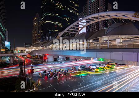 Chong Nonsi Skywalk - beleuchtete Fußgängerzone, Wolkenkratzer und Stau im zentralen Geschäftsviertel der Innenstadt in Bangkok, Thailand in der Abenddämmerung Stockfoto