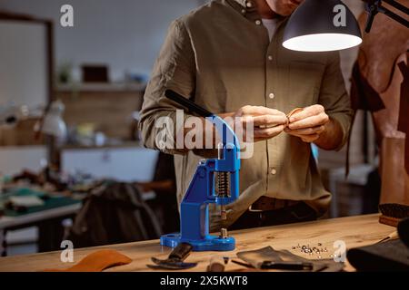 Maschine für die Herstellung von geprägten Logobuchstaben auf Lederprodukten, die das Klischee erhitzt und das gewünschte Bild auf das Material drückt, Handwerker im Hintergrund des Fotos. Nahaufnahme zugeschnittener Shot Stockfoto