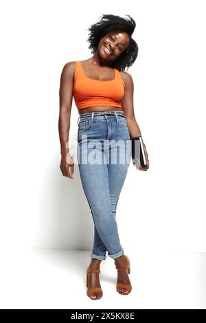 Studio-Porträt einer lächelnden Frau in orangefarbenem Oberteil und Jeans Stockfoto