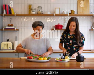 Mutter und Erwachsene Tochter schneiden Gemüse in der Küche Stockfoto