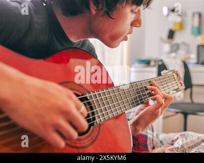 Nahaufnahme eines Teenagers, der Akustikgitarre auf dem Bett spielt Stockfoto