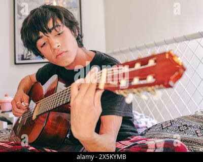 Teenager spielt Akustikgitarre auf dem Bett Stockfoto