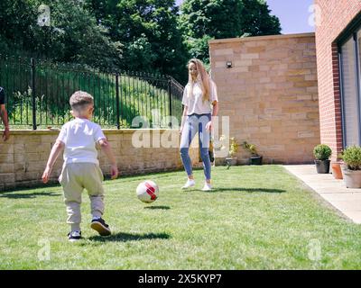 Mutter mit Sohn spielt Fußball im Hinterhof Stockfoto