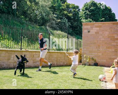 Vater spielt mit Kindern und Hund im Hinterhof Stockfoto