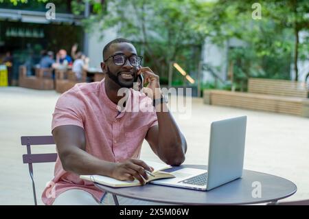 Mann mit Smartphone und Laptop, der am Tisch im Straßencafé arbeitet Stockfoto