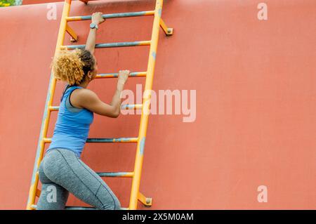 Sportliche, junge Frau, Kletterleiter Stockfoto